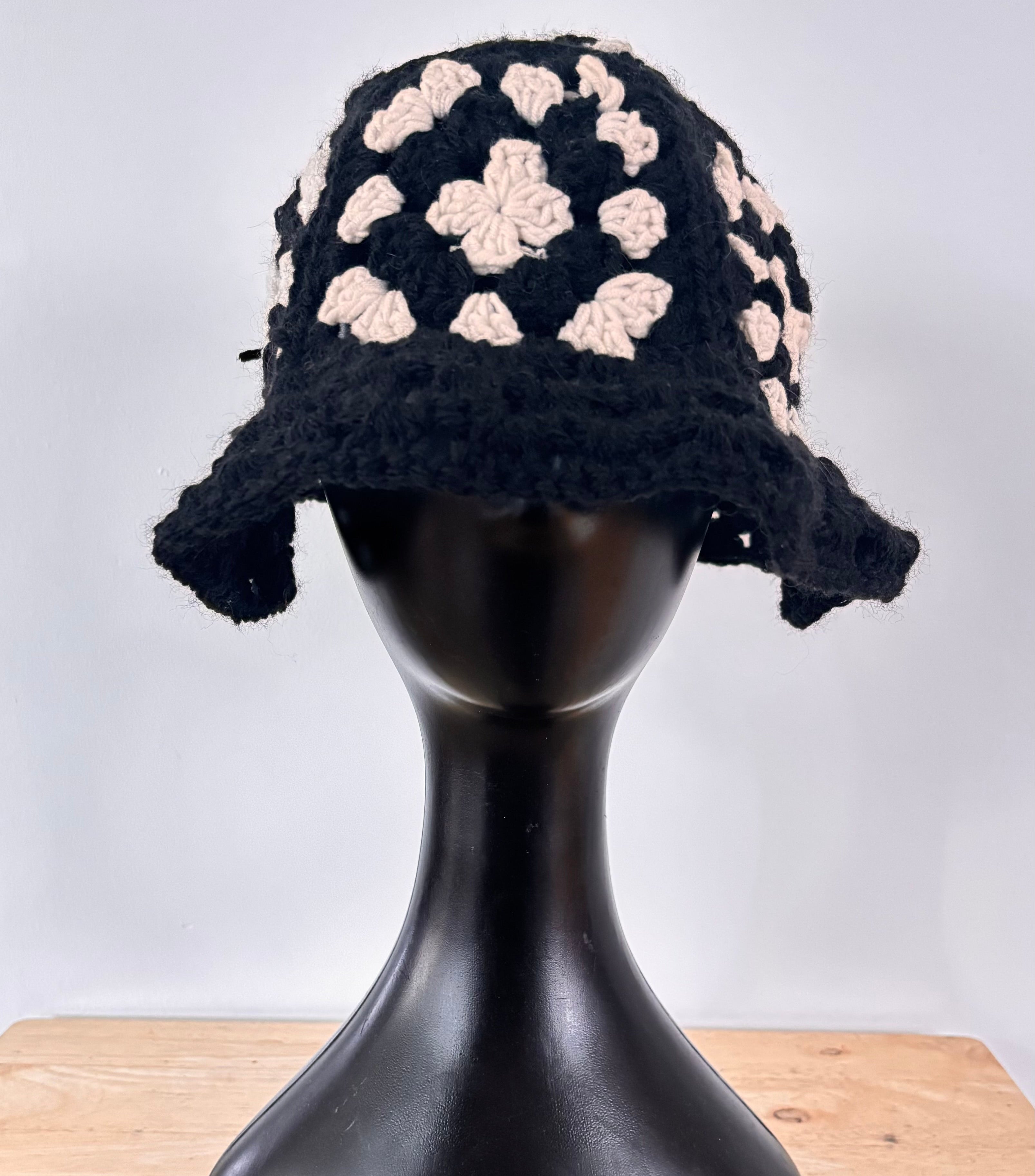 Black and white crochet hat on a black mannequin head against a white background