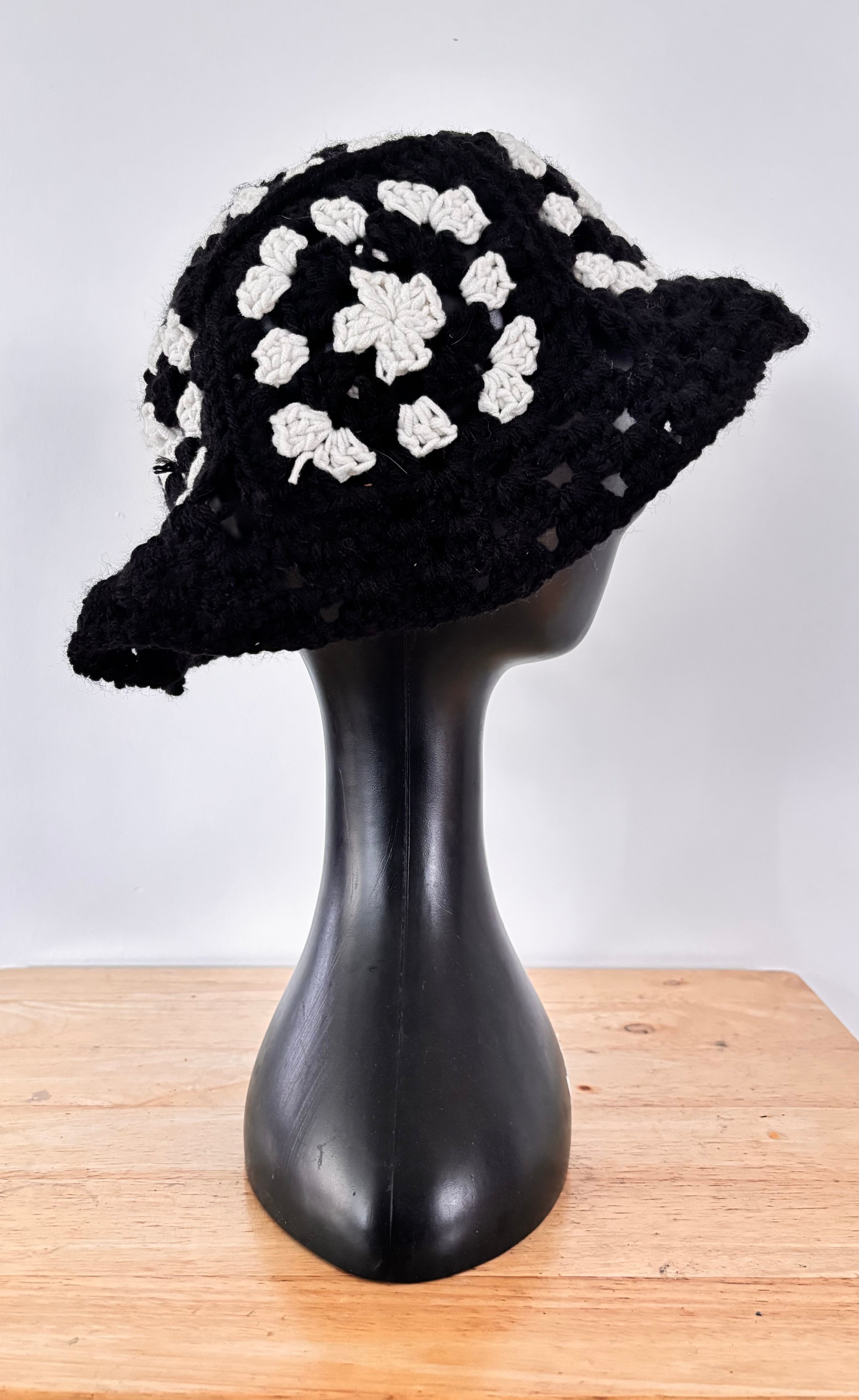 Black crochet hat with white patterns on a mannequin head against a white background