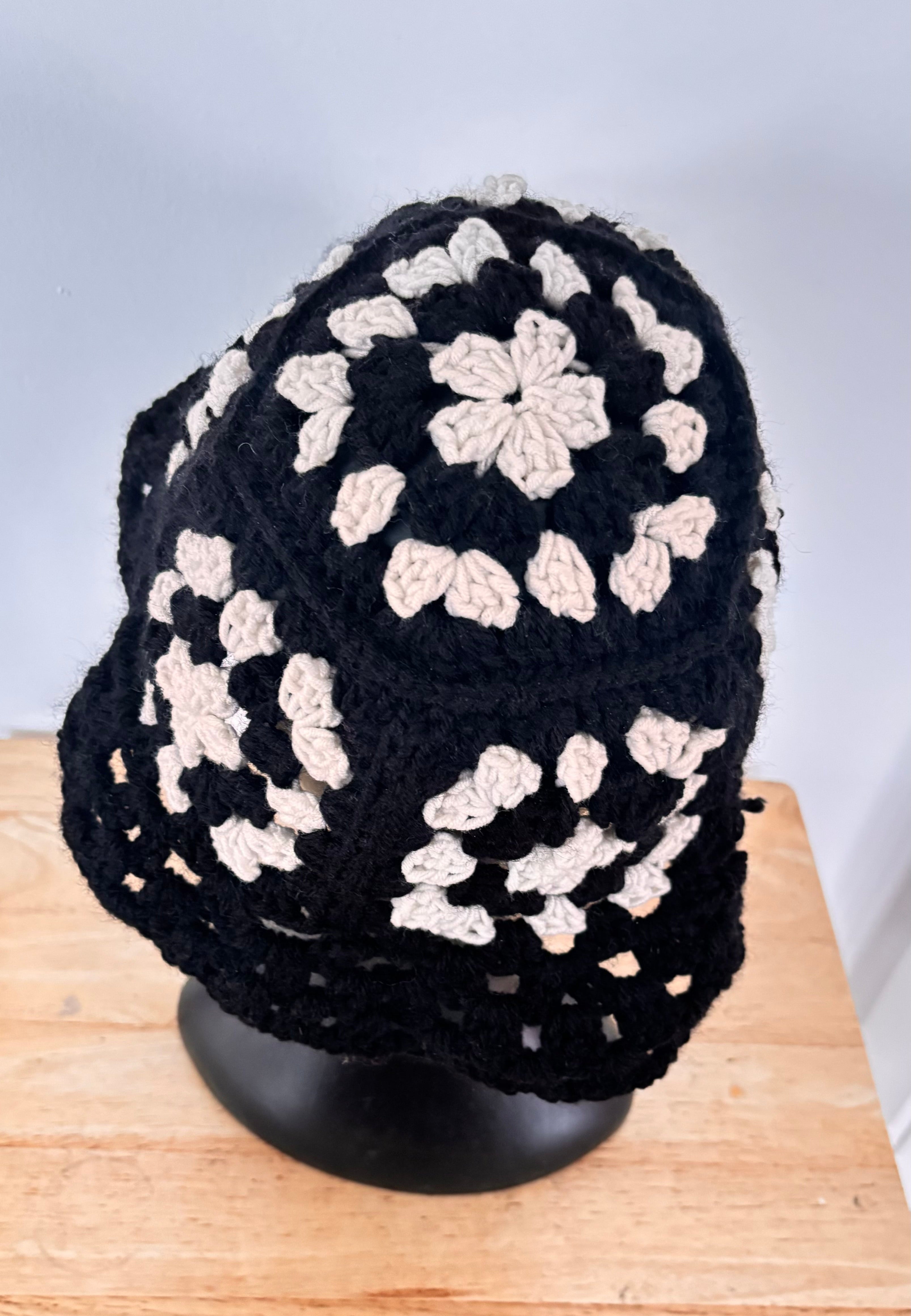 Black and white crocheted hat on a wooden surface with a light gray background