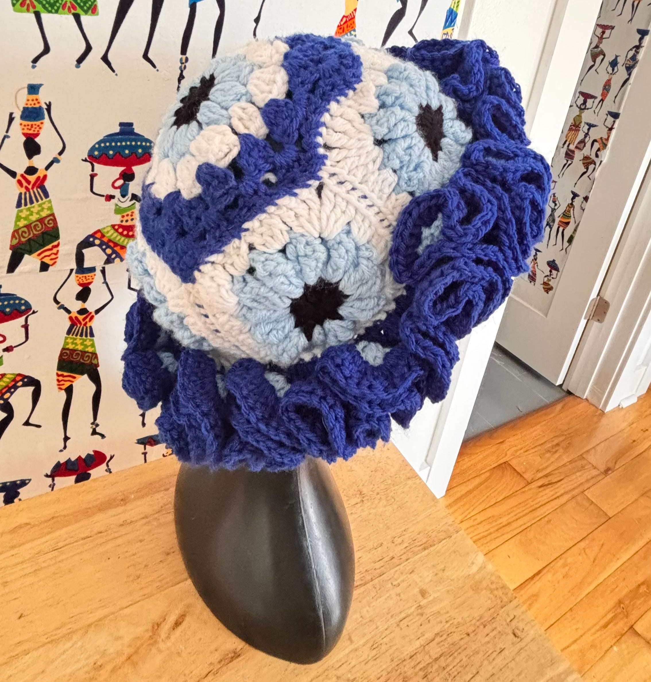 Blue and white evil eye granny square bucket crocheted hat on a mannequin head with a colorful background