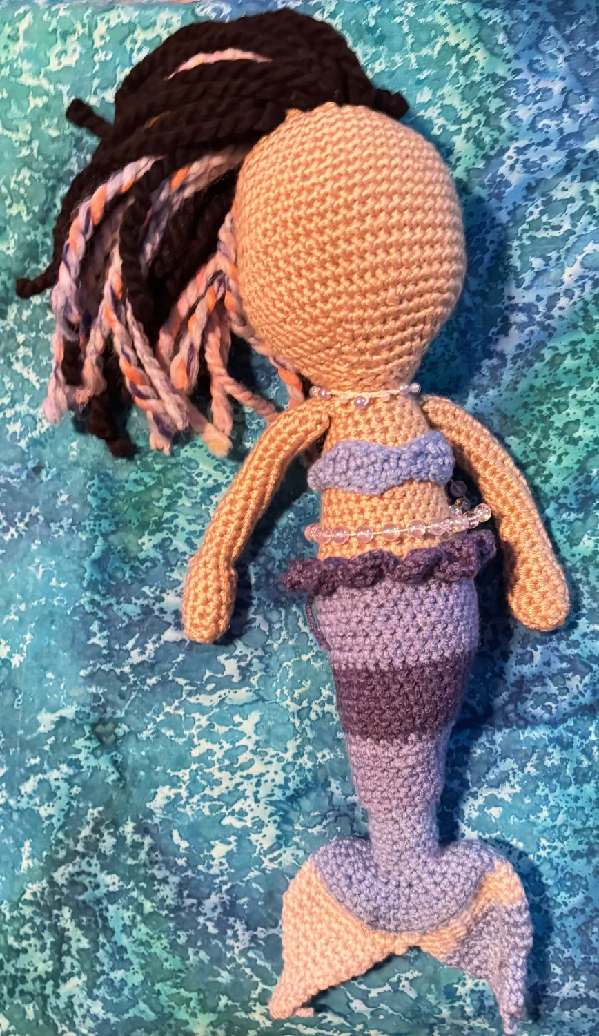Crocheted mermaid doll on a textured blue fabric background
